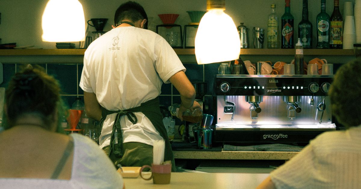 A barista skillfully prepares coffee at the espresso machine in a warmly lit café environment.